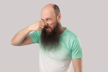 Bad smell. Portrait of confused middle aged bald man with long beard in light green t-shirt...