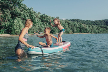Caucasian woman parent riding kids children boys on paddle sup surfboard in water. Modern outdoor...