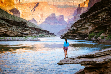 A woman watches sunrise light the cliffs, Colorado River, Grand Canyon National Park, Arizona, USA