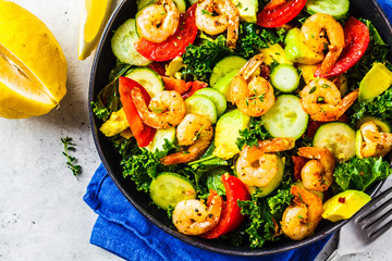 Shrimp, avocado and vegetable salad in a black dish on gray background, top view.