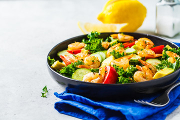 Shrimp, avocado and vegetable salad in a black dish on gray background.