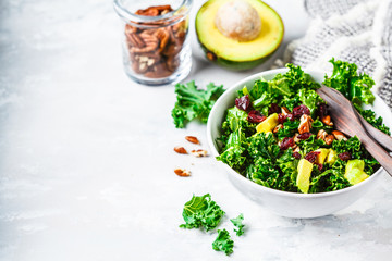 Green kale salad with cranberries and avocado in white bowl. Healthy vegan food concept. - obrazy, fototapety, plakaty