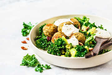 Vegan lentils meatballs with green kale salad, avocado and tahini dressing in a white dish.