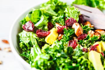 Green kale salad with cranberries and avocado in white bowl. Healthy vegan food concept.