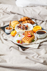 Breakfast with oatmeal, waffles, coffee, croissants and fruits in bed.