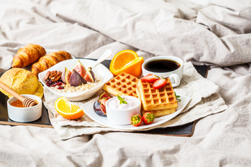 Breakfast with oatmeal, waffles, coffee, croissants and fruits in bed.