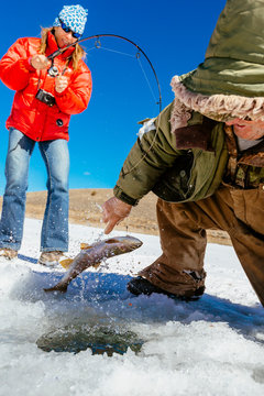A man is teaching a woman to fish for trout on iced over Panguitch Lake, Dixie National Forest, Utah, USA