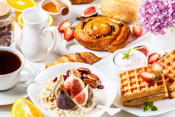 Breakfast table with oatmeal, waffles, croissants and fruits.