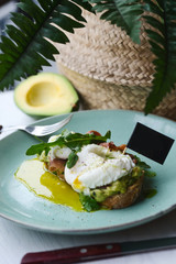 Hot toast with jamon, poached egg, herbs and avocado on a plate with a black copy space flag on a skewer