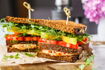 Vegan sandwich with tofu, hummus, avocado, tomato and sprouts.