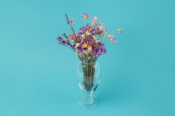 Beautiful bouquet of dried cornflowers in a glass vase on a turquoise background