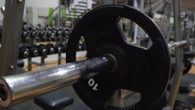 Male hands place weight on bar in gym securing it with spring clasp - close up, camera slide
