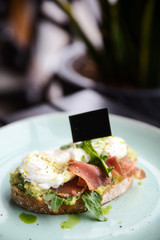 Hot toast with jamon, poached egg, herbs and avocado on a plate with a black copy space flag on a skewer