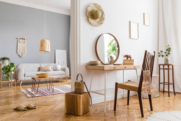 Modern and design home interior of open space with wooden desk, coffee table, sofa, chair, plants, mirror, macrame and elegant accessories. Stylish and minimalistic home decor. Template. Bright rooms.