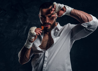 Handsome brutal man in protective boxing gloves is vering mouth guard while posing for photographer.