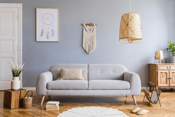 Stylish and design home interior of living room with gray sofa, wooden cube, commode, pillow, macrame, rattan lamp, basket, plants and elegant accessories. Stylish home decor. Template. Mock up poster