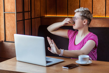 Obraz premium bad smell. Portrait of unhappy confused young woman with short hair in pink t-shirt and eyeglasses is sitting in cafe, covering nose with finger and pleased to stop and pinching her nose. indoor