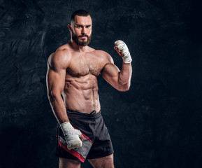 Fototapeta na wymiar Muscular handsome fighter with naked torso is demonstraiting his power at dark photo studio.