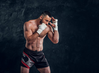 Strong muscular fighter is showing his punch while posing for photographer at dark photo studio.