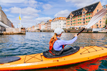 A woman is paddling a sea kayak past the entrance to historic Nyhavn in the canals of Copenhagen, Denmark.