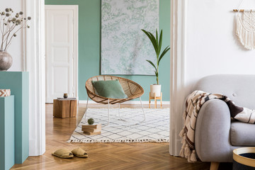 Modern and bohemian composition of interior design at apartment with gray sofa, rattan armchair, wooden cubes, plaid, tropical plant, macrame and elegant accessories. Stylish home decor. Template.