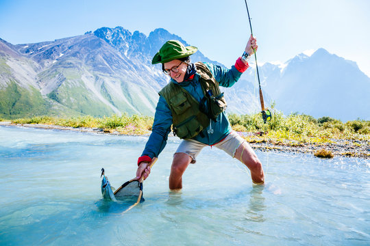 A man with a grayling caught while fly fishing on Turquoise Lake in Lake Clark National Park and Preserve, Alaska, USA