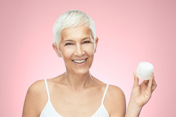 Gorgeous smiling Caucasian senior woman trying out new anti age cream and looking at camera. Beauty...