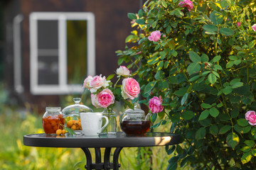 Jam in glass jar. Romantic dinner in the garden under a rose bush.