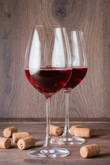 Two glasses with red wine and cork on a wooden table