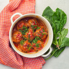 Meatballs stewed in tomato sauce in a saucepan with spinach and dill