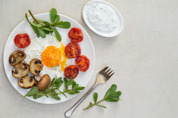 Fried eggs, tomatoes, mushrooms with purslane and sauce on a white plate