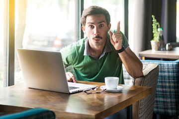 Oh, I have an idea! Young surprised businessman in green t-shirt sitting with idea gesture and...
