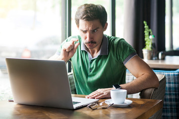 Give me a few more. Young businessman in green t-shirt sitting and looking at laptop display on...