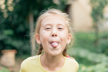 Blond little girl with yellow green eyes sticking out her tongue