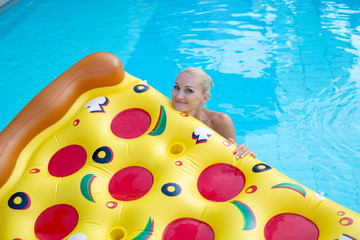Beautiful girl sits in a pool on a pizza-like air bed in a scarlet swimsuit