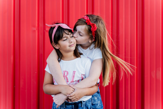 Two sisters standing in front of a red wall, kissing