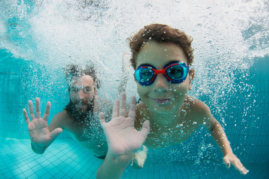 Happy family father witswimming under water in pool during summer vacation