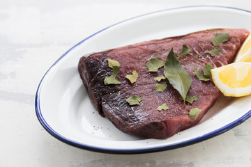 raw tuna with lemon and bay leaf on ceramic background