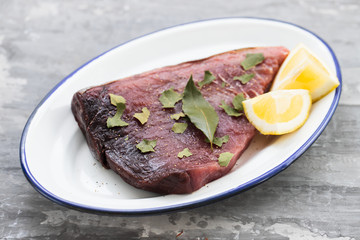 raw tuna with lemon and bay leaf on ceramic background