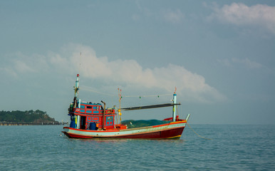 Close up of red fishing boat with fishnet moored in the calm sea near the beach