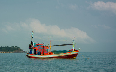 Fototapeta premium Close up of red fishing boat with fishnet moored in the calm sea near the beach