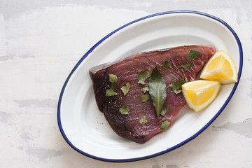 raw tuna with lemon and bay leaf on ceramic background