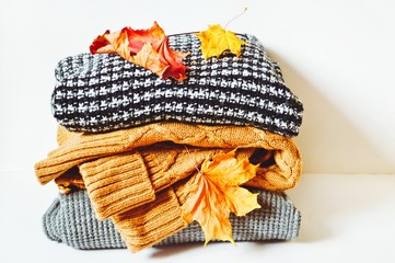Fototapeta na wymiar Cold weather women's clothes. Pile of woolen clothing. Striped, brown, gray woolen knitted sweaters and yellow and red maple leaves