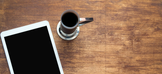White digital tablet on a wooden table with a cup of coffee. Copy space. Banner