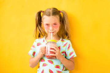 Smiling girl drinking fresh watermelon smoothie on yellow background