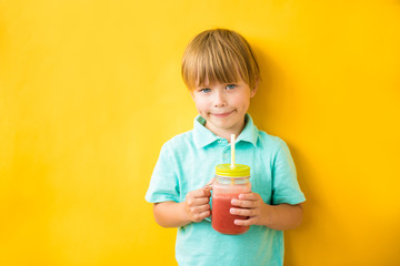 Smiling child boy holding a fresh smoothie on a yellow background