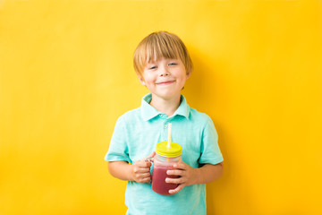 Smiling child boy holding a fresh smoothie on a yellow background