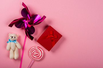Pinwheel, teddy bear, lollipop and gift on pink background. Space for text on the right side of the image.