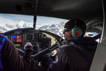 A man in the copilot seat of a small plane above the Alaska Range of mountains over Denali National Park, USA