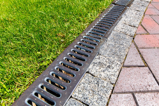 iron grate of a drainage system for storm water drainage from a pedestrian sidewalk near a green lawn.